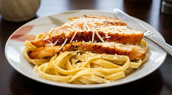 Fettuccine Alfredo with sliced chicken breast and shredded Parmesan cheese on a white plate.