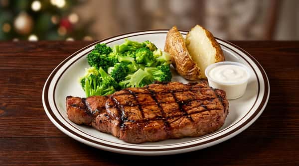 Grilled steak with grill marks, a baked potato half, steamed broccoli, and a side of sour cream on a white plate.