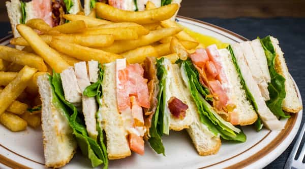 Club sandwich with white bread, sliced chicken, bacon, lettuce, tomato, and mayonnaise, served with golden french fries.