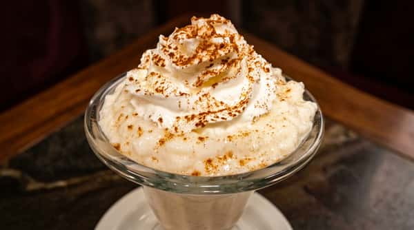 Rice pudding with a swirl of whipped cream and a dusting of cinnamon in a clear glass dish.