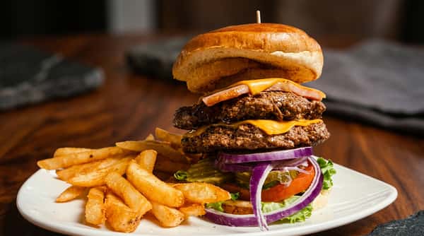 Double cheeseburger with fries, lettuce, tomato, onion, and pickles on a white plate.