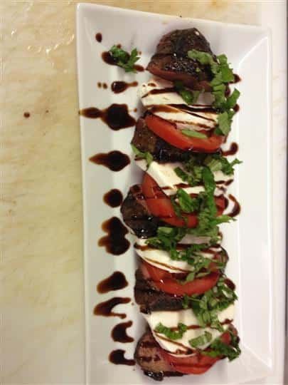 Beef on a platter topped with vegetables and sauce