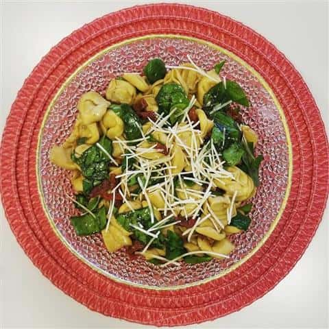 A dish filled with tortellini pasta and spinach topped with cheese.