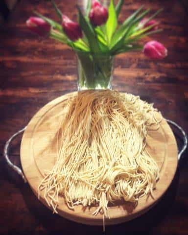 A plate of spaghetti next to a vase of flowers.
