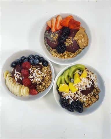 Three different acai bowls topped with a variety of fruits.