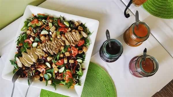 A salad topped with grilled chicken, tomatoes, croutons and a variety of vegetables.