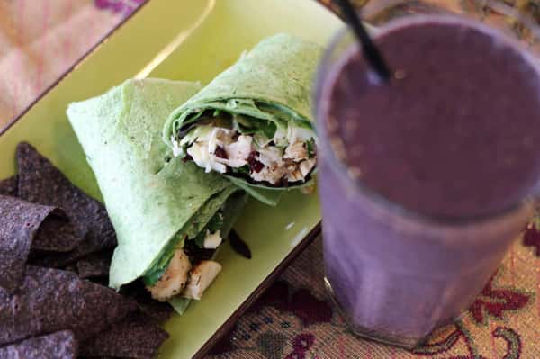 A spinach wrap filled with grilled chicken, cheese and lettuce, next to a smoothie.