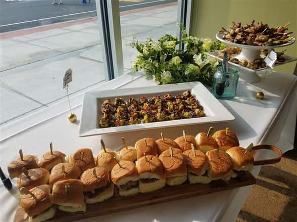 A tray of hamburger sliders next to other platters of food.