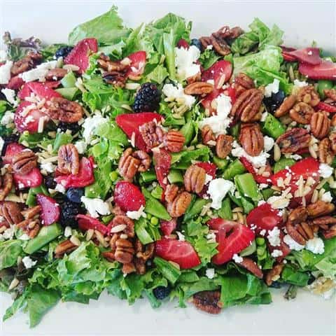 A salad with chopped walnuts and berries topped with cheese.