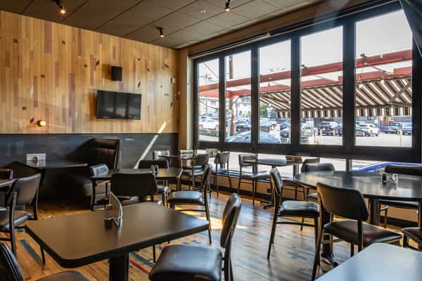 Spacious and modern interior of Rookies Sports Bar and Grill with wooden accents, wall-mounted TV, black dining tables, and large windows offering street views and natural light.