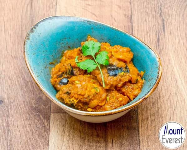 Bowl of creamy orange curry with vegetables, topped with fresh cilantro and served in a blue ceramic bowl on a wooden table.