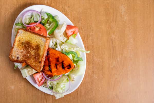 Grilled chicken salad with lettuce, tomato, cucumber, peppers and toast, viewed from above.
