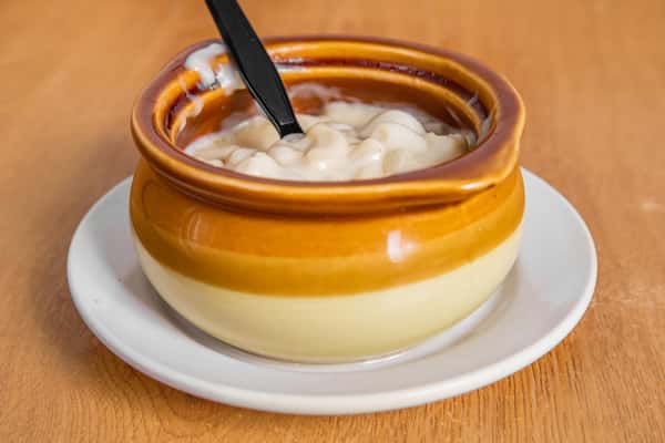 Macaroni and cheese in a brown crock on a saucer with a black spoon.