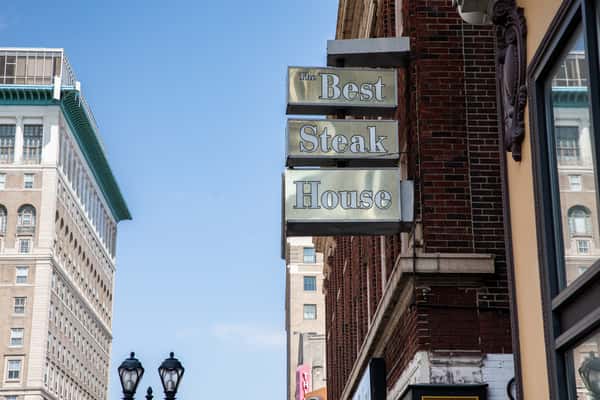 The Best Steak House sign above the sidewalk, viewed against a blue sky.
