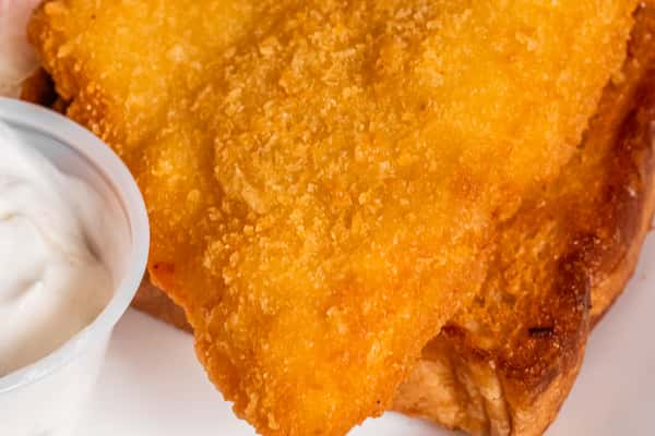 Close-up of a golden breaded fish fillet with a cup of sauce at the edge of the plate.