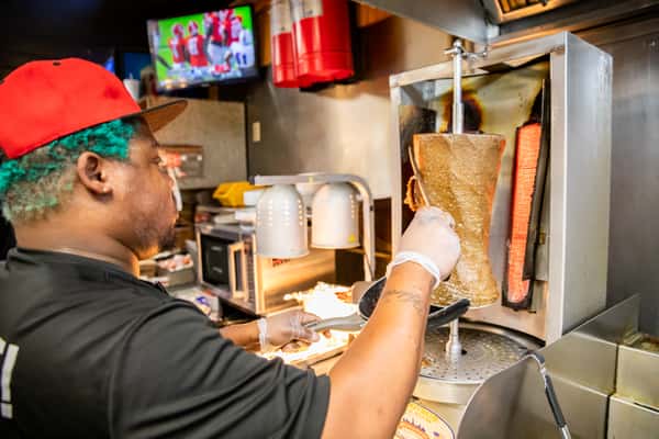Staff member carving gyro meat from a vertical rotisserie.