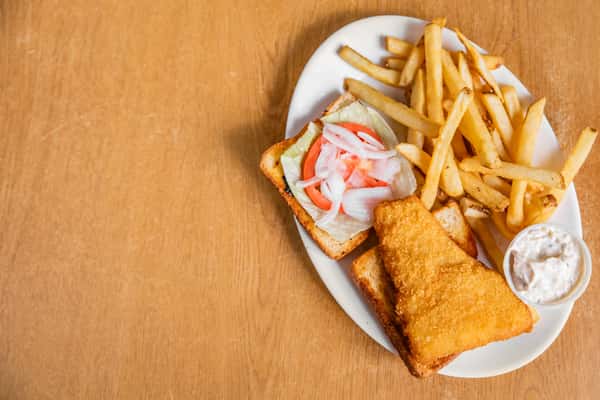 Fish sandwich on toast with fries, lettuce, tomato, onion and sauce on an oval plate.