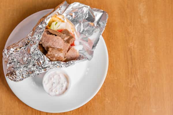 Gyro in an open foil wrapper with a cup of sauce, viewed from above.