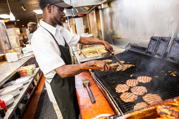 Cook using tongs over a smoky grill filled with steaks and patties.