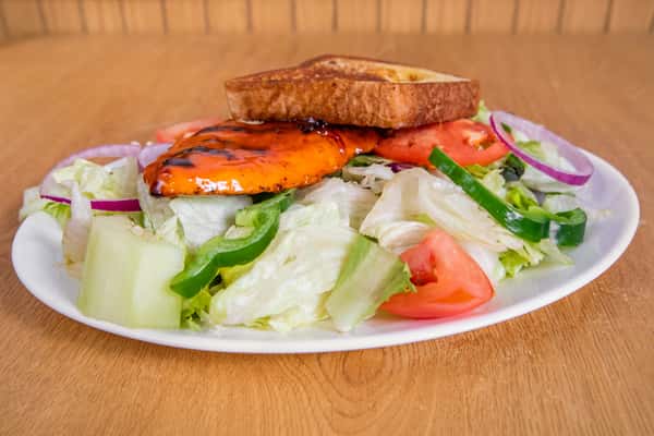 Grilled chicken salad topped with toast, with lettuce, tomato, cucumber and peppers.