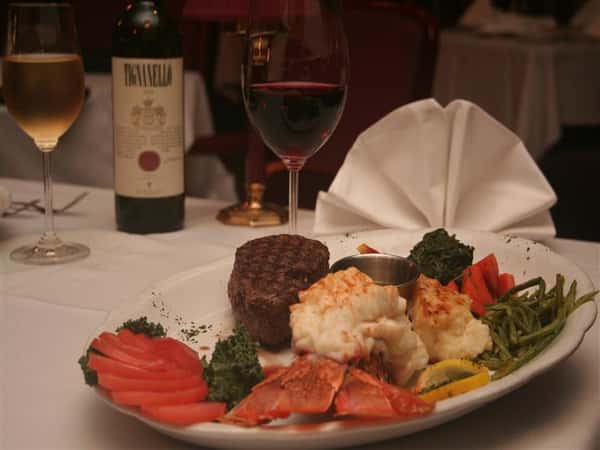 lobster and steak cooked on a plate with a glass of red wine.