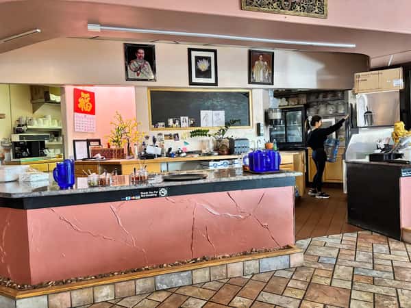 Interior of a Thai restaurant featuring a service counter with condiments, blue water pitchers, decorative portraits, and a staff member changing a water jug.