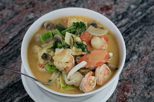 Rice noodles in a large bowl topped with a red Curry sauce that has coconut milk, broccoli, cabbage, bell pepper, onions, carrots, basil & mushrooms.