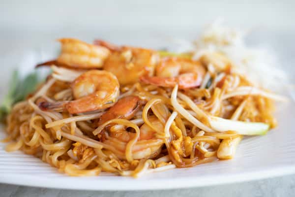 Close-up of shrimp pad thai with rice noodles, bean sprouts, egg, and scallions served on a white plate.