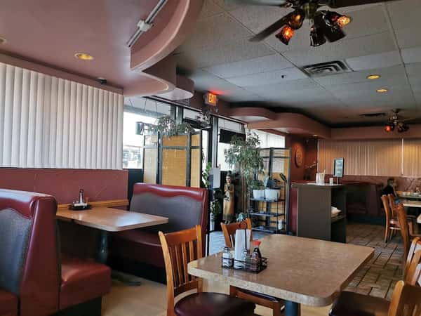 Cozy Thai restaurant interior with maroon booths, wooden tables, dim lighting, and a decorative Buddha statue near the entrance.