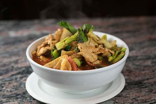 Stir-fried rice noodles served in a large bowl Covered in a spicy sauce with broccoli, cabbage, bell pepper, onions, carrots, mushrooms & basil.