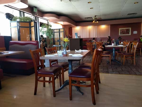 Spacious Thai restaurant dining area with wooden chairs, maroon booths, and soft lighting; decorated with plants and a Buddha statue.