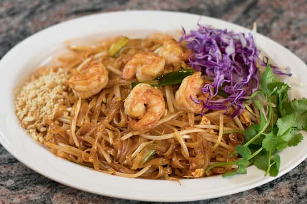 Shrimp Pad Thai with rice noodles, bean sprouts, crushed peanuts, purple cabbage, and cilantro on a white plate.