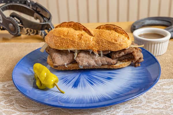 Toasted French dip sandwich with thin-sliced roast beef and grilled onions on a crusty roll, served with au jus and a pepperoncini.