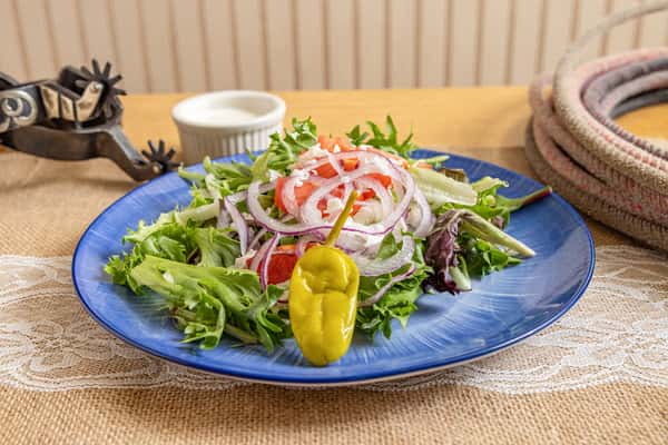 Fresh garden salad with spring mix greens, sliced tomatoes, red onions, and a pepperoncini, served on a blue plate with ranch dressing on the side.