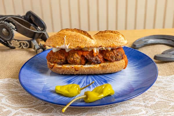 Hearty meatball sub sandwich with marinara sauce and melted cheese on a toasted hoagie roll, served with pepperoncini on a vibrant blue plate.
