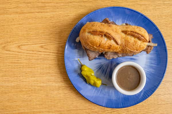 Classic French dip sandwich with sliced roast beef on a toasted hoagie, served with au jus dipping sauce and a pepperoncini on the side.