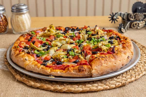 Vegetarian pizza with black olives, green bell peppers, diced tomatoes, onions, and marinated artichokes on a tomato sauce base, served on a rustic woven mat.