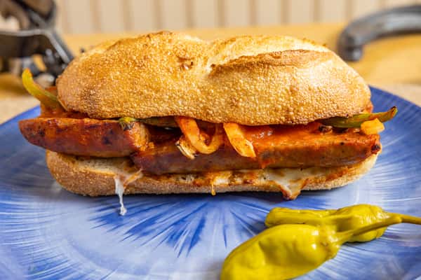 Grilled sausage and pepper sandwich with melted cheese and marinara, served on a toasted hoagie roll with pepperoncini on the side.