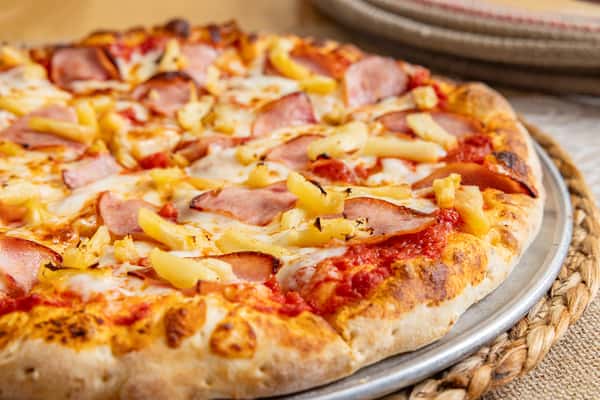 Close-up of a Hawaiian pizza topped with Canadian bacon and pineapple chunks on a golden, hand-tossed crust.