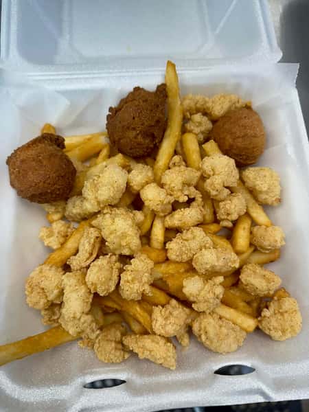 A white takeout box filled with crispy fried shrimp pieces, golden french fries, and brown hushpuppies from Seafood Shack & More.