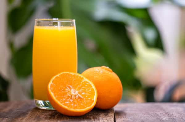 Glass of fresh orange juice with whole and sliced oranges in the background.