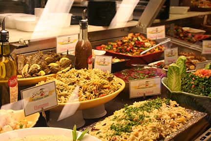 a buffet table filled with entrees and sides such as rice, pasta salad, greek salad, and peppers and onions