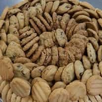 Large platter of assorted freshly baked cookies including chocolate chip, peanut butter, sugar, and sandwich cookies, arranged in a circular display, showcasing a variety of homemade gourmet bakery treats with golden-brown textures perfect for dessert catering or sweet tables.