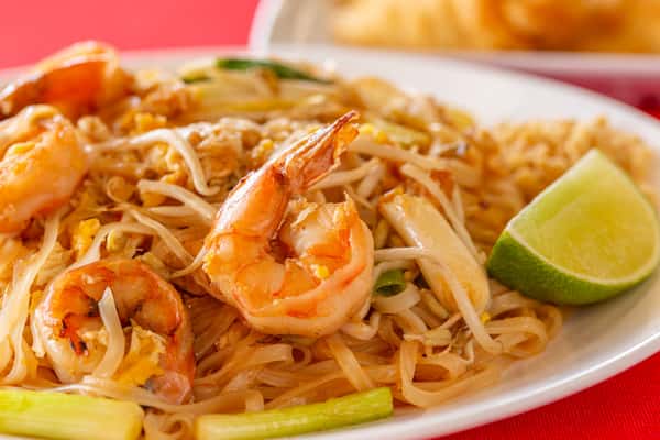 Shrimp pad Thai with rice noodles, bean sprouts, scallions, scrambled egg, and lime wedge on a white plate.