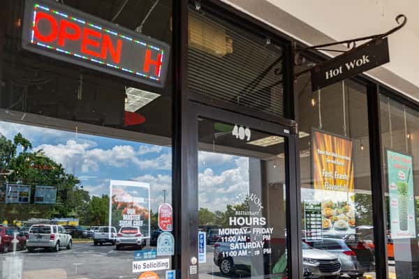 Close-up view of the Hot Wok restaurant entrance, showcasing business hours, promotional posters, and an "Open" sign—perfect for local SEO and business directory listings.
