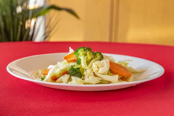 Stir-fried mixed vegetables with broccoli, carrots, cabbage, and onions on a white plate with crispy egg rolls in the background.