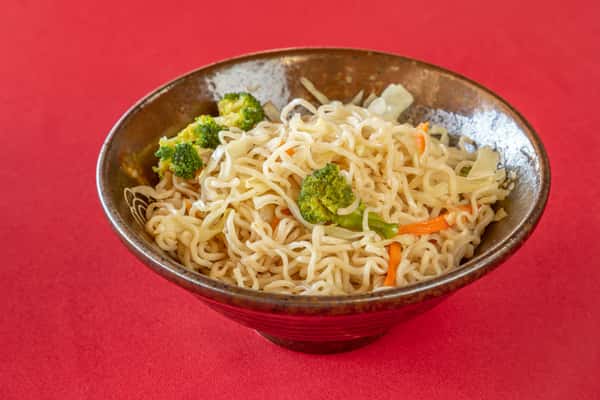 Stir-fried noodles with broccoli, cabbage, and carrots served in a rustic ceramic bowl on a red tabletop.