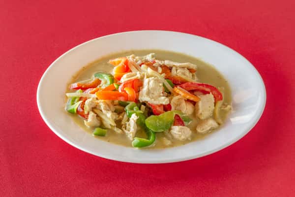 Stir-fried Thai green curry chicken with colorful bell peppers, onions, and carrots in a creamy coconut-based green curry sauce, served on a white plate atop a red tablecloth.