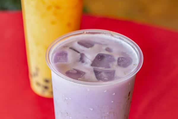 Iced taro milk tea with chewy boba pearls, served in a clear plastic cup over a red tablecloth—classic purple bubble tea made with creamy taro root and ice cubes.