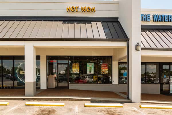 Street view of Hot Wok restaurant storefront in a strip mall, featuring bold signage and large front windows with promotional posters for dine-in and takeout Asian cuisine. Ideal for local SEO and business listings.